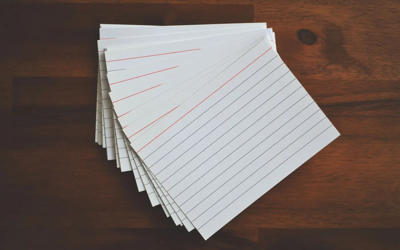 A fanned stack of blank ruled index cards on a dark wooden table