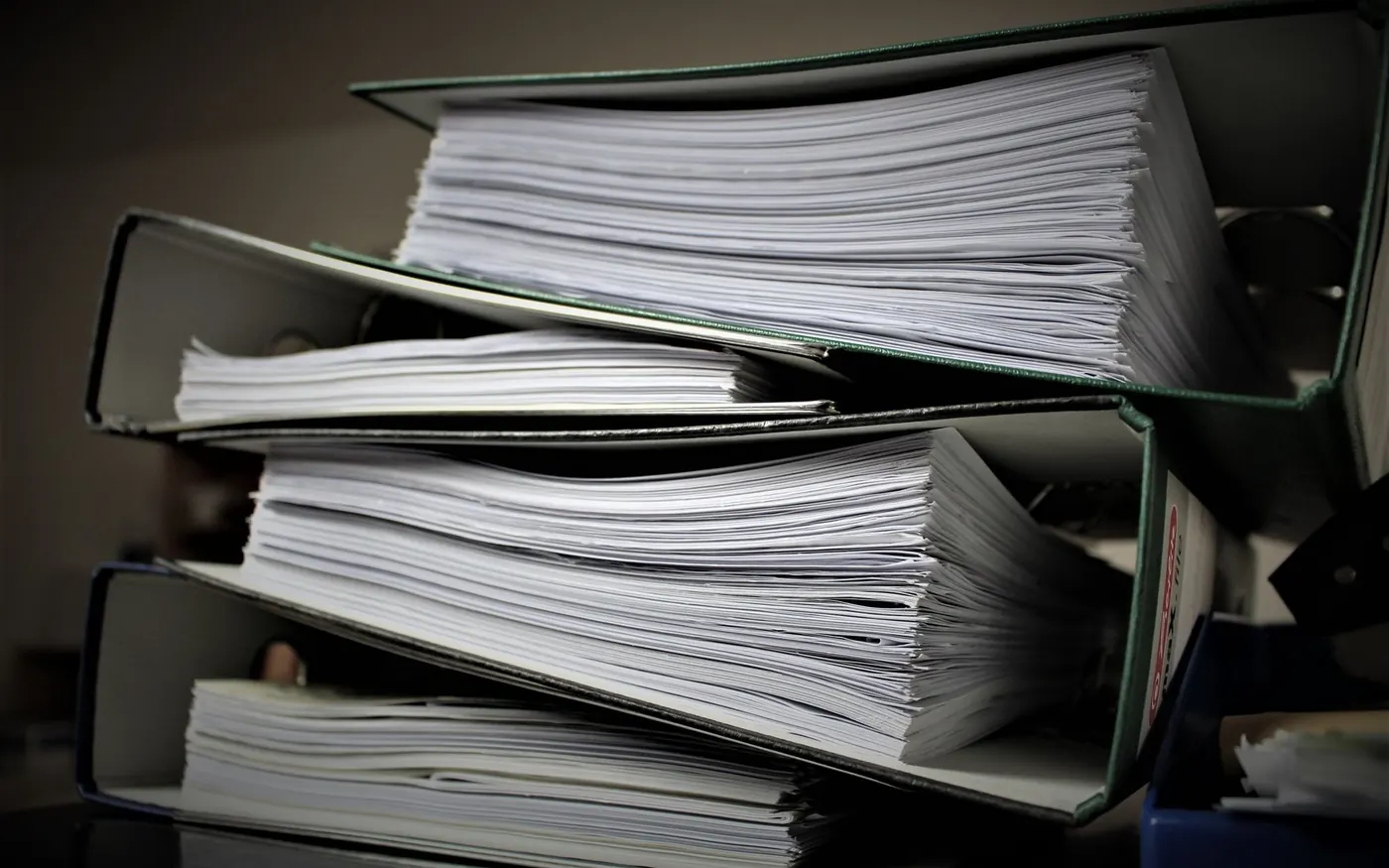 Thick ring binders full of paper files stacked on top of each other